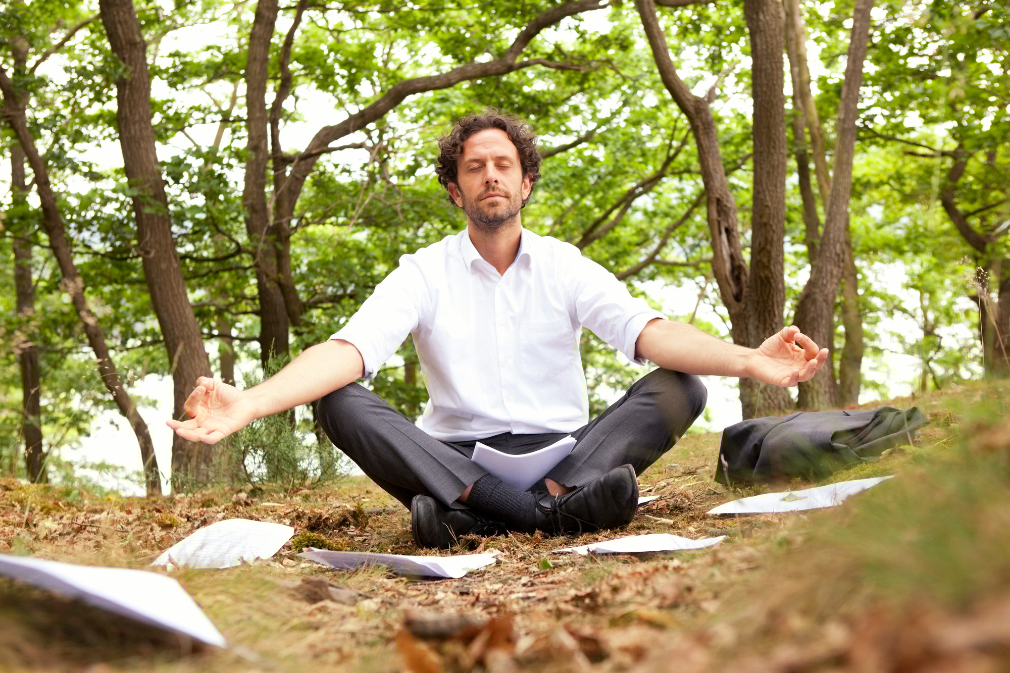 Germany, businessman in forest surrounded by papers practising yoga