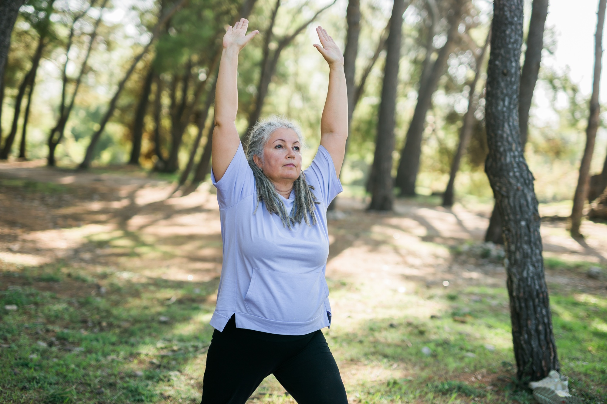 Mature elderly grey haired dreadlocks woman training in park, doing yoga or fitness - wellbeing and