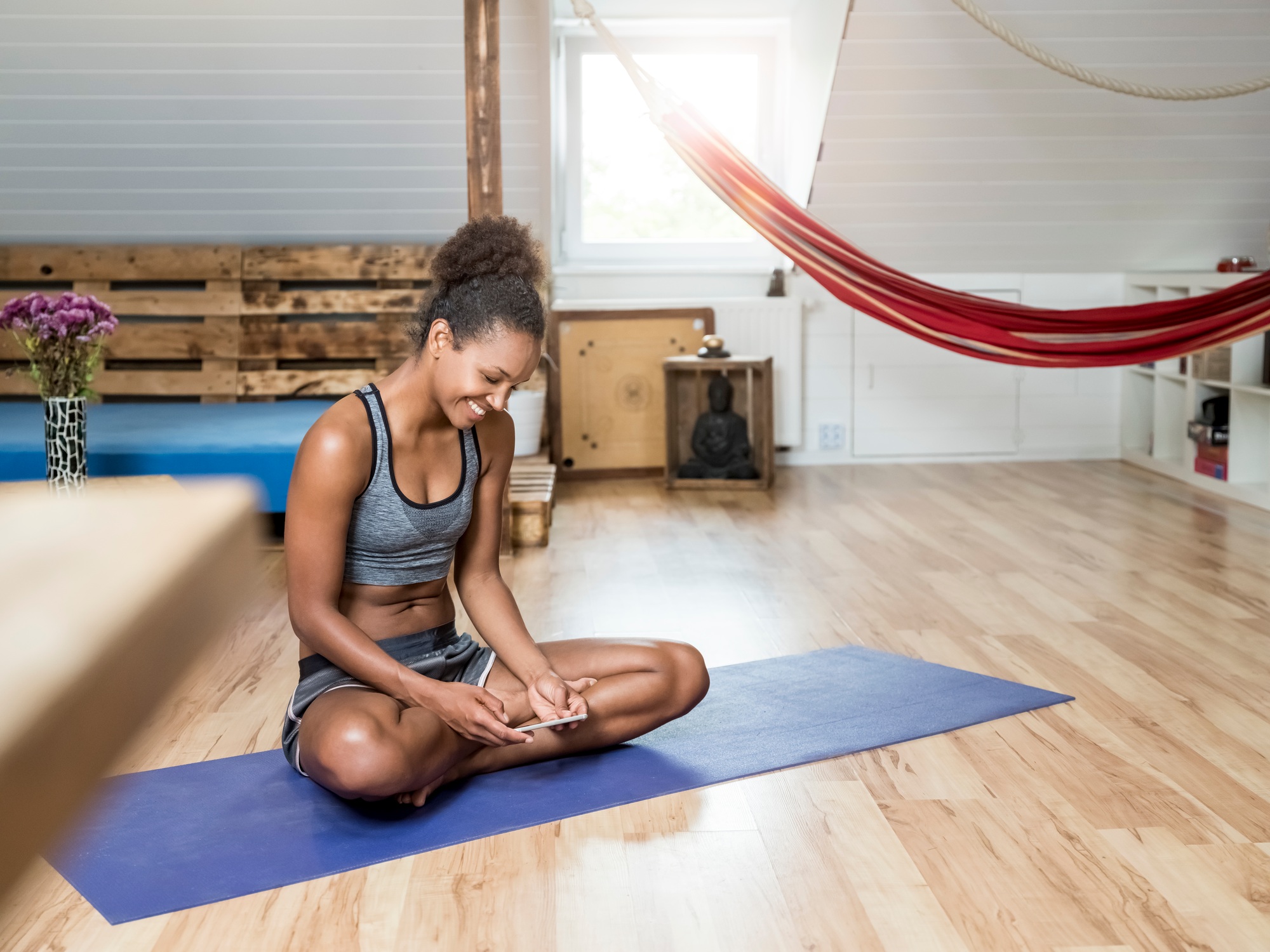 Smiling young woman sitting on yoga mat looking at cell phone